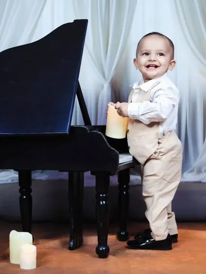 A happy toddler stands by the piano in a smart outfit during his music-themed session.