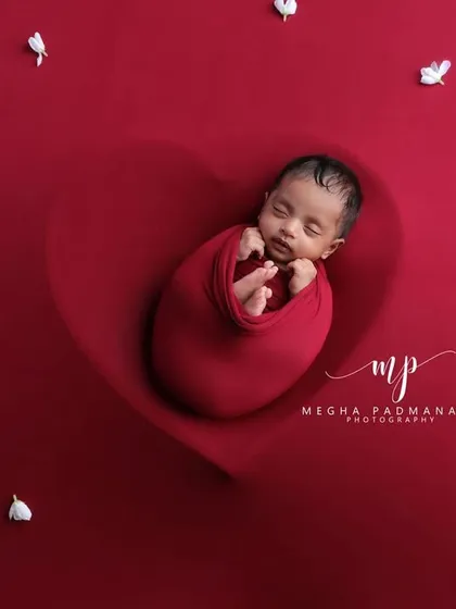 A wide shot of the baby in a red heart prop, surrounded by delicate white petals, creating a beautiful and artistic composition.