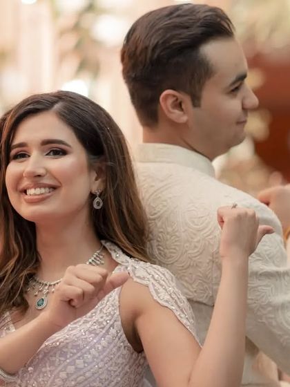 A fun shot of the bride, back to back with her groom, smiling and pointing at him playfully.