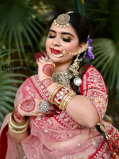 A playful and happy shot of a model in our red and pink lehenga, showing off her henna-adorned hands.