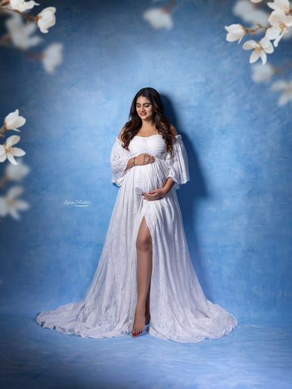 A moment of quiet connection, framed by delicate white blossoms. The off-the-shoulder lace gown adds a touch of romance to this serene, sky-themed portrait.