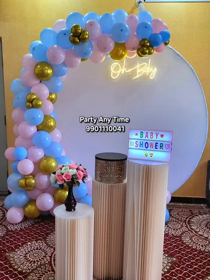 Celebrating a new arrival is a special moment. I design beautiful baby shower setups like this one with a round backdrop, a pink, blue, and gold balloon arch, and an 'Oh Baby' neon sign to welcome the little one.