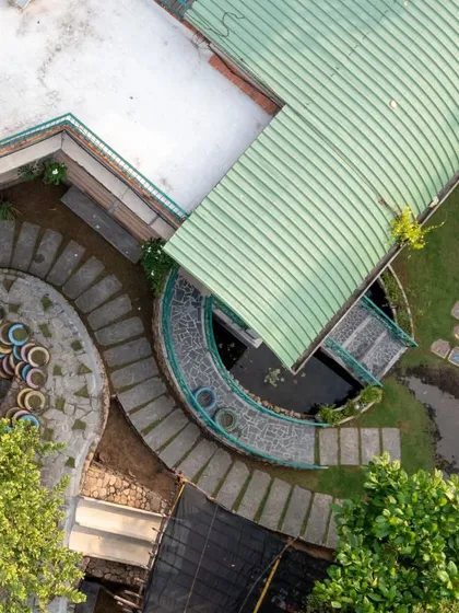 The design incorporates curved pathways and green roofs that follow the natural contours of the land. This top-down view highlights the use of recycled tires for seating and the careful integration of walkways, water features, and plant life.
