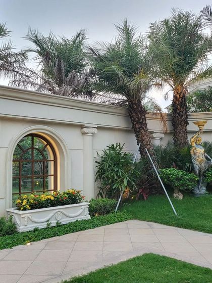 A corner of a classical garden featuring an arched window, stone planter box, and a graceful sculpture. The thoughtful placement of these elements creates a rich, layered, and timeless aesthetic.