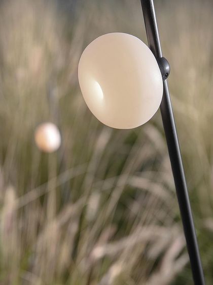 A close-up of a single Firefly light, its simple, spherical form looking like a dewdrop on a blade of grass.