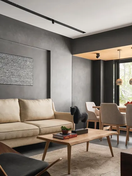 This living space from the Zen House shows a complete composition of custom and curated furniture. The light wood coffee table, neutral sofa, and sculptural armchair create a calm, balanced atmosphere against the textured concrete walls.