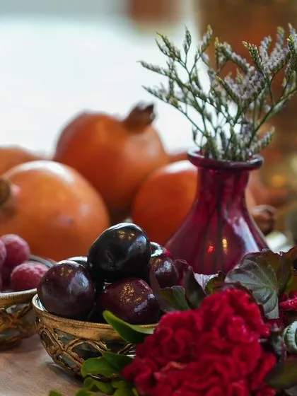 A detail shot of fresh raspberries and plums in small brass bowls, placed next to pomegranates. The use of fresh, seasonal fruit adds a layer of authenticity and sensory appeal.