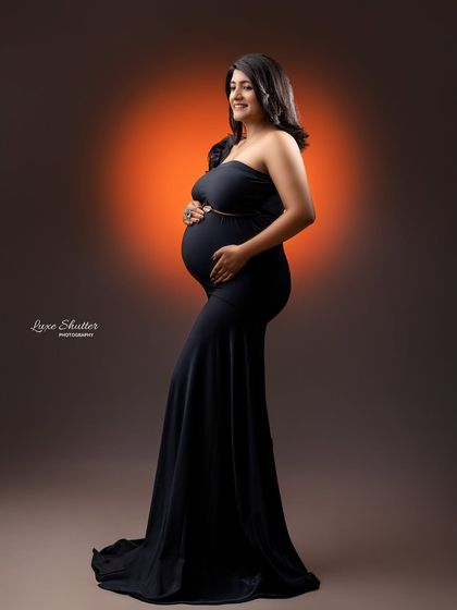 A profile view in a classic black gown, with a warm light creating a beautiful rim light effect that highlights the baby bump.