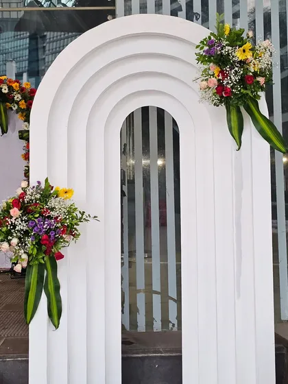 A modern, white arched entryway panel used as part of the event decor. The clean, tiered design is accented with two asymmetrical bouquets of colorful fresh flowers, adding a contemporary touch to the formal setting.