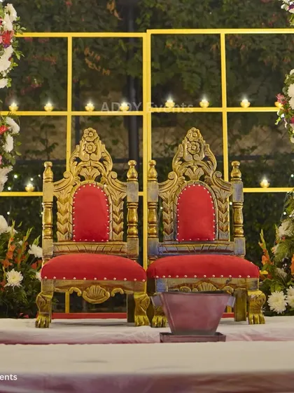 The thrones for the king and queen of the day. These ornate, golden chairs with rich red upholstery are the perfect regal seating for the bride and groom within the mandap.