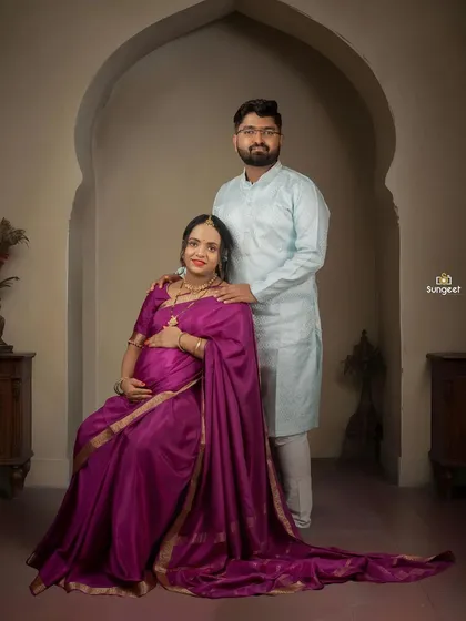 A formal seated portrait of the couple. The husband stands protectively beside his wife, creating a classic and dignified family picture.