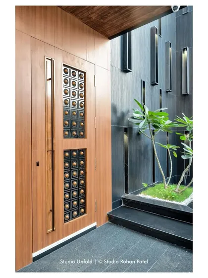 A detail of the main door, which features intricate metalwork, set against a dark, textured wall with linear light fixtures.
