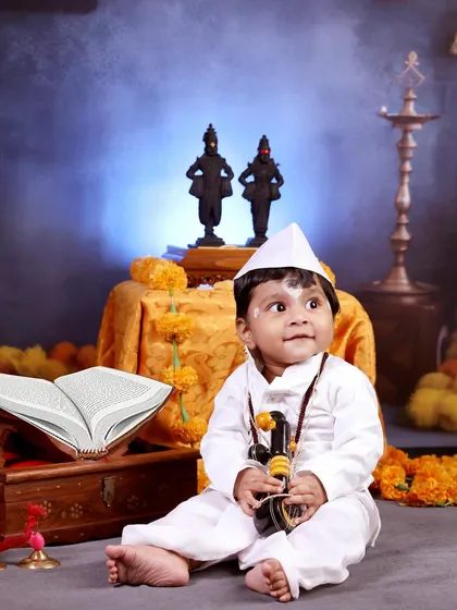 A 10-month-old boy dressed as a little Warkari, sitting with a miniature ektara in front of Vitthal-Rakhumai idols.