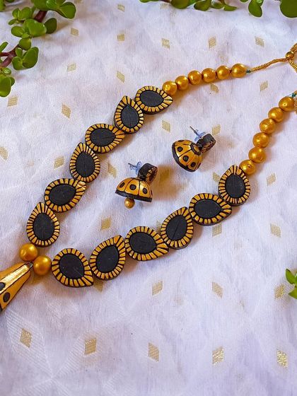 A sleek and beautiful necklace in black and gold. The chain is made of oval beads, leading to a unique hanging pendant, and it comes with matching jhumkas.