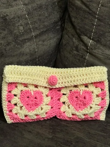 The finished granny square heart pouch. This handmade clutch features two pink hearts and a simple button closure, making it a great multi-purpose bag.