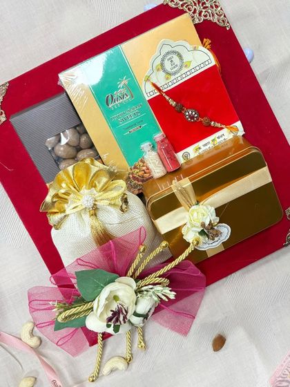 A Rakhi gift hamper presented in a luxurious red tray. This arrangement includes a mix of sweets, savory snacks, and a beautiful rakhi, all elegantly packed and ready for gifting.