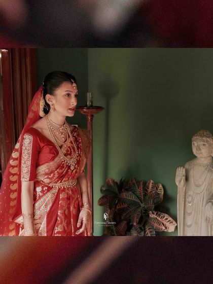 A serene portrait of the bride in her red saree, looking out from a doorway.