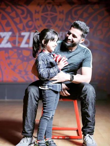 A heartwarming moment between a trainer and his daughter at the studio. We are a family-friendly space where fitness is a shared passion across generations.