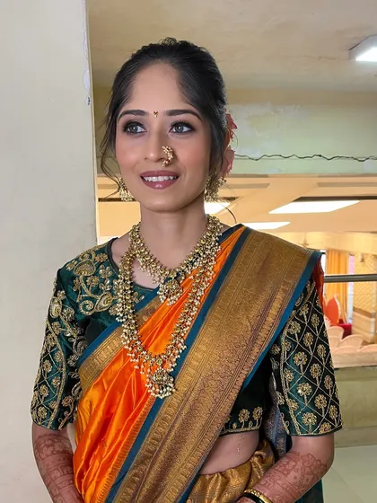 A full shot of the bride, showing her beautiful orange and green saree and a simple, elegant hairstyle.