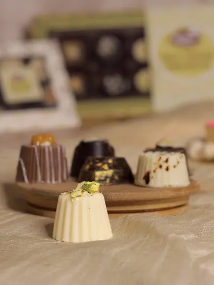 A closer look at our soft-center chocolates, each one a unique flavor experience. This assortment features our Pista Kunafa chocolate, a white chocolate shell filled with a nutty, textured center, alongside other decadent varieties.