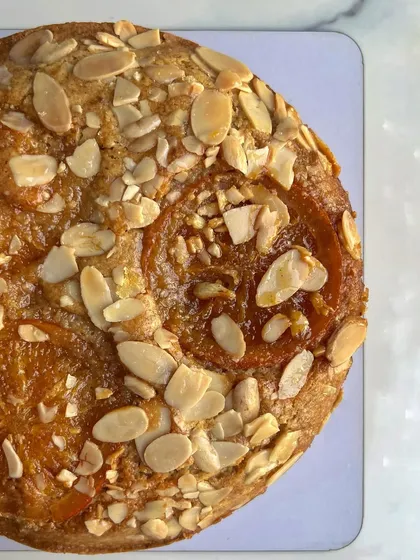 A top-down view of my orange and almond tea cake. It's a simple, buttery cake topped with candied orange slices and toasted almond flakes. It's rustic, elegant, and so delicious.