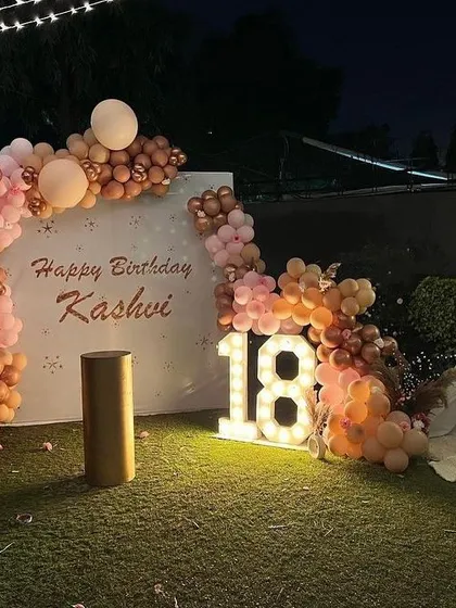 Here’s a chic 18th birthday I decorated on a terrace. I used marquee light-up numbers and a custom backdrop with the birthday person's name, framed by a stylish organic balloon arch in peach and rose gold tones for a sophisticated evening celebration.
