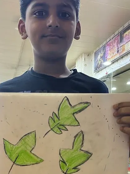 A student proudly displays his drawing of green leaves. Even simple subjects can become beautiful pieces of art.