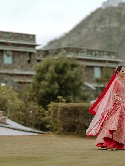 A wide shot of the bride in her red lehenga against the backdrop of the Ramada resort in Udaipur, showcasing the scale of the destination.