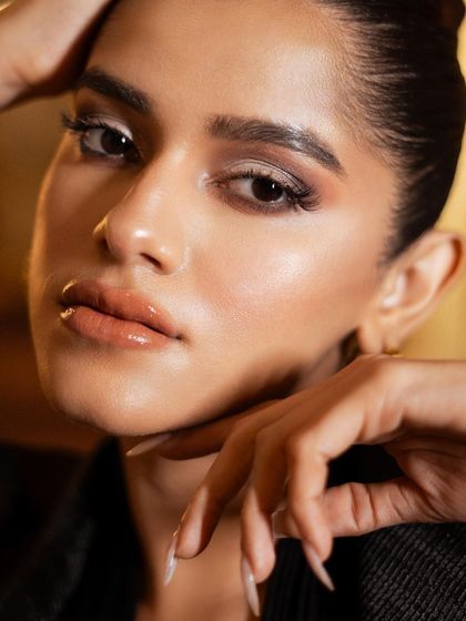 A detailed beauty close-up. The soft, warm lighting beautifully illuminates the model's flawless makeup and the texture of her skin, creating a luxurious and polished look.
