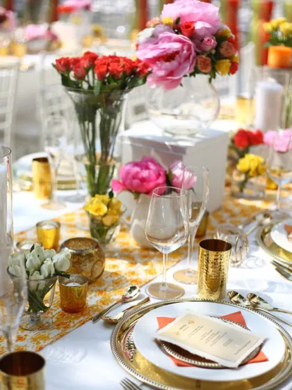 A bright and cheerful daytime wedding lunch setup. The vibrant floral centrepieces and gold accents create a warm and inviting atmosphere for guests to celebrate.