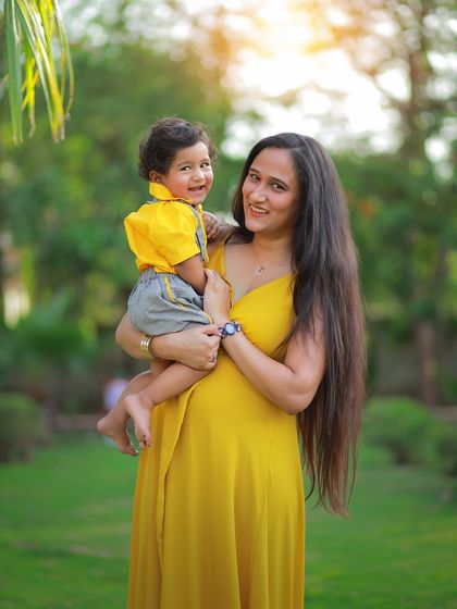 A mother and her son share a beautiful smile in this sun-kissed outdoor portrait. The warm light and natural green background create a perfect setting for family photos.