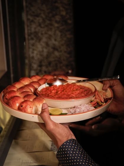 A server presents our signature Pav Bhaji. The aroma of the spiced vegetable mash and buttery, toasted buns is irresistible.