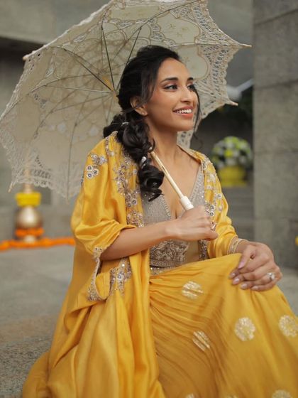 A playful shot of the bride with a vintage umbrella. The makeup is fresh and dewy, perfect for a daytime Haldi function.