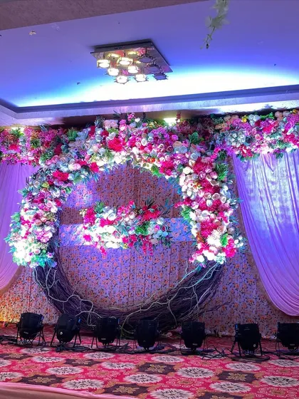 A rustic yet elegant stage featuring a large crescent-shaped wreath made of woven branches and covered in a cascade of colorful flowers.