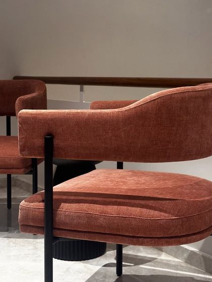 A closer view of the statement chair, showing the texture of the rustic orange fabric and the gentle curve of the backrest. This piece is designed for both comfort and visual appeal.