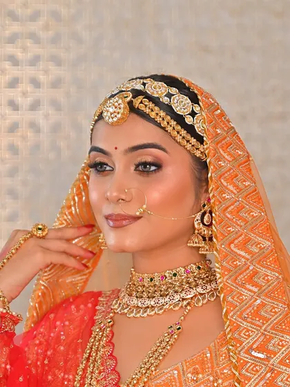The epitome of bridal grace. The bride's look is completed with a beautiful orange bandhani dupatta over her head, framing her face and highlighting her flawless makeup.