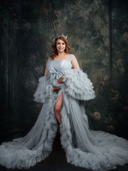 A regal portrait featuring a stunning grey ruffled gown and a crown. The dark, painterly backdrop adds a touch of royal elegance, making this a truly majestic maternity photograph.