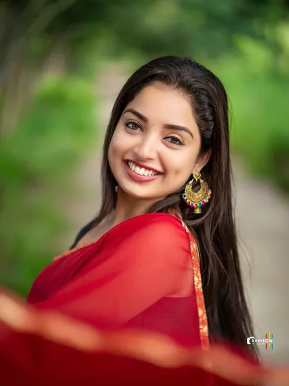 The same sheer red saree, but this time with a bright, engaging smile directed at the camera. This shows how a simple change in expression can alter the mood of a portrait.