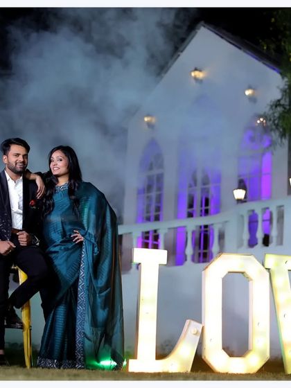 This pre-wedding shot has a cool, stylish vibe. The couple's pose is confident and relaxed, and the purple backlighting on the white building adds a touch of modern glamour.