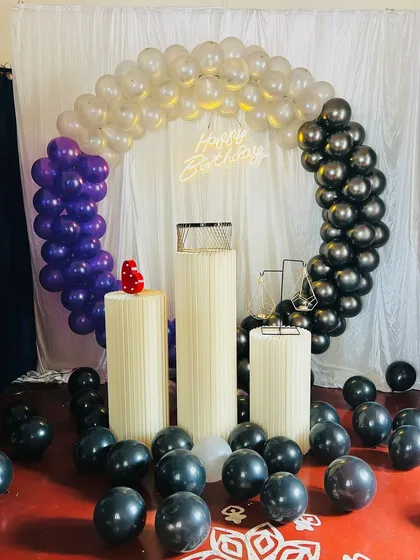 A birthday decoration with a unique color combination of transparent, purple, and black balloons. The balloons scattered on the floor add to the celebratory feel.