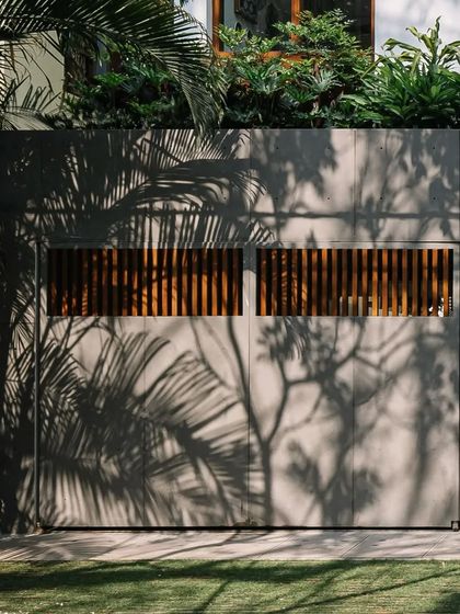 The play of shadows from tropical foliage on the home's concrete and wood facade creates a living, changing pattern throughout the day.