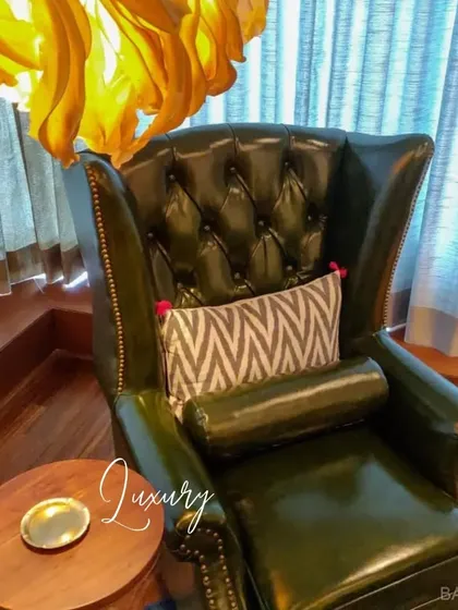 A close-up of a luxurious tufted leather wingback chair, paired with a simple wooden side table. A perfect example of classic comfort.