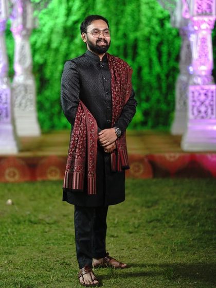 A full-length view of the black Jodhpuri and shawl combination. The client is wearing traditional footwear which completes this ethnic look for a wedding guest.