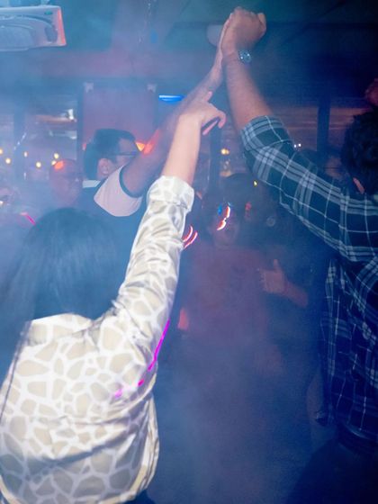 Two people with their hands up, united by the music in a smoke-filled club.
