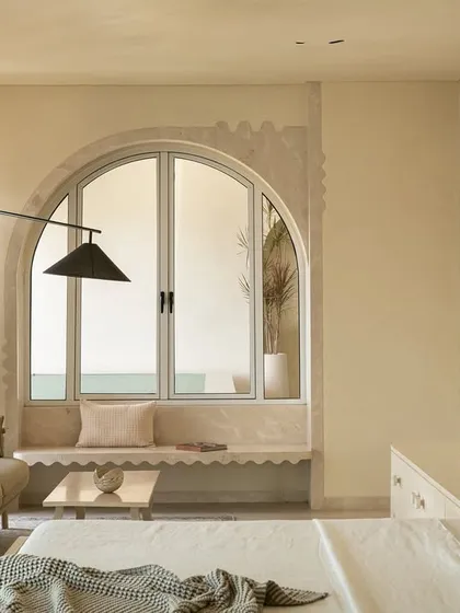 The master suite in the 'Soft Serve' project is enveloped in a timeless taupe. The custom bed and vanity feature abstract patterns in Movingue White veneer, with scalloped motifs framing the bay window.