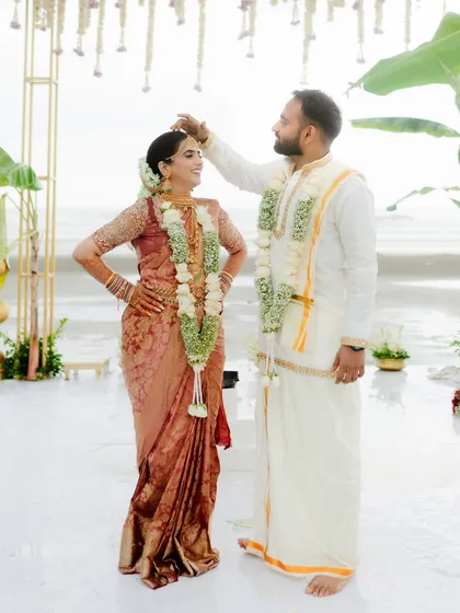 A playful and tender moment under the mandap, as the groom adjusts something on the bride's head. Their easy chemistry is evident.