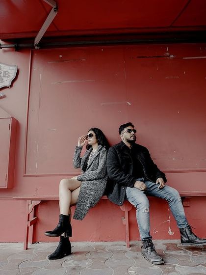 A wide shot of a couple sitting back-to-back on a red bench, creating a stylish and symmetrical urban portrait.