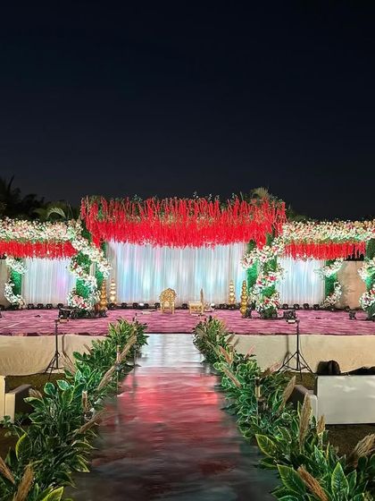 A wider perspective of the red and green themed reception stage, showing the guest seating arrangement and the impressive scale of the outdoor setup.