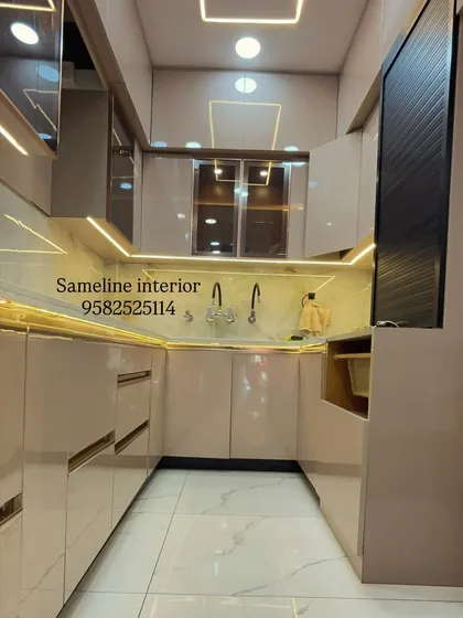 A full view of a U-shaped modular kitchen we delivered to a client. The design uses glossy beige cabinets with gold profile handles and extensive under cabinet and ceiling lighting for a bright, luxurious feel.