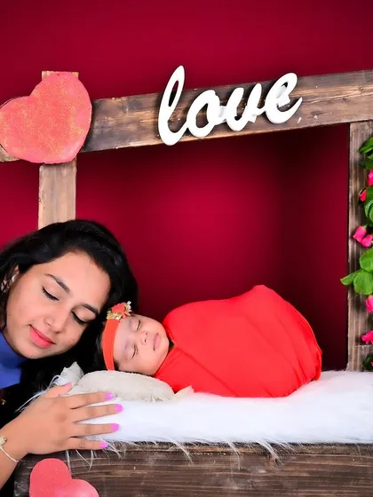A mother gently resting her head next to her sleeping newborn in a "love booth" setup.